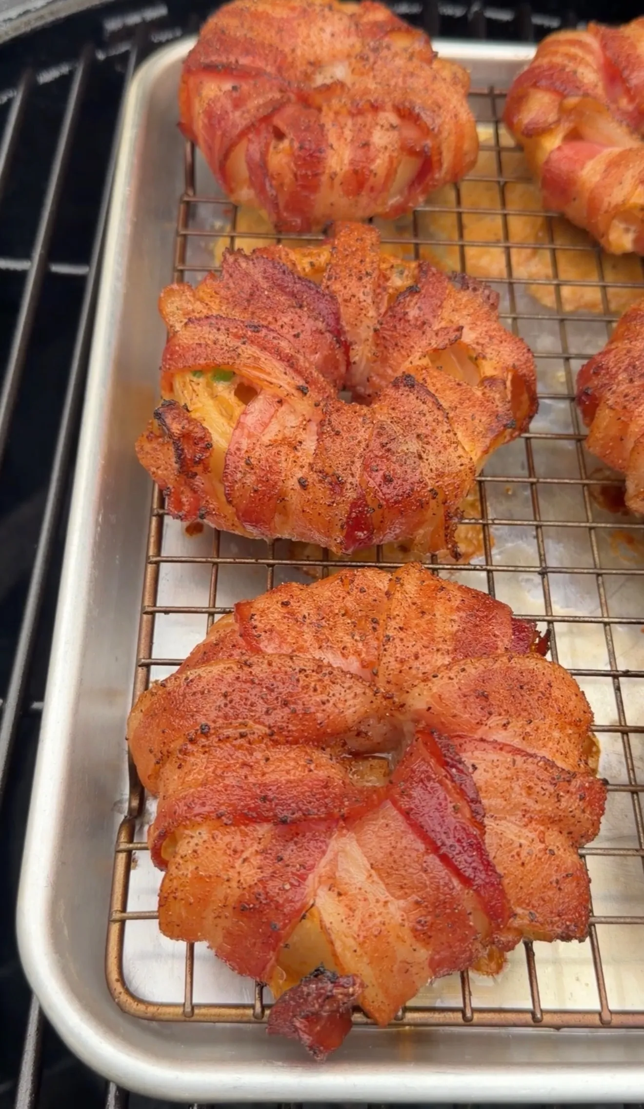Crab stuffed bacon-wrapped onion rings with seasoning on a wire cooling rack in baking pan