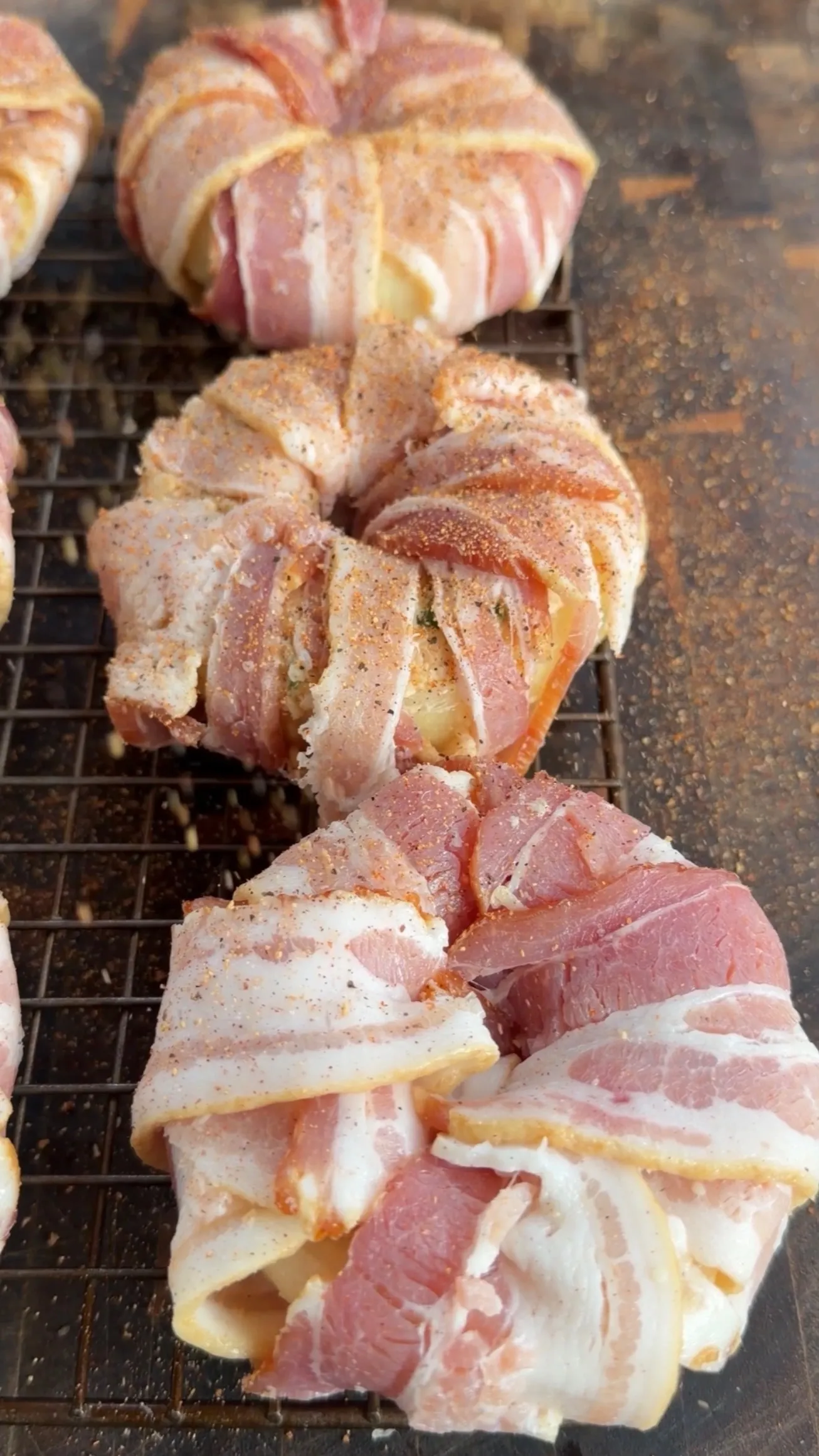 Bacon-wrapped crab stuffed onion rings cooking on a metal grill grate, seasoned and browning