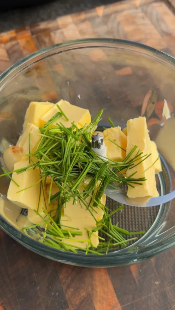 Butter cubes and fresh green herbs in a clear glass food processor bowl for steak stuffed bread boat recipe