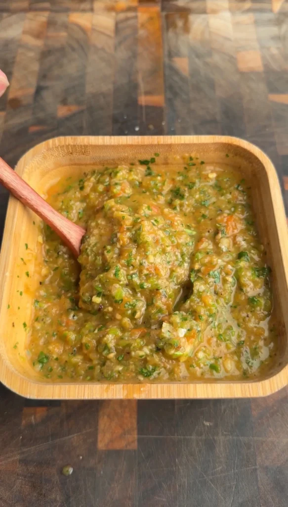 Chunky charred salsa verde with fresh herbs in a square wooden bowl with wooden spoon on cutting board