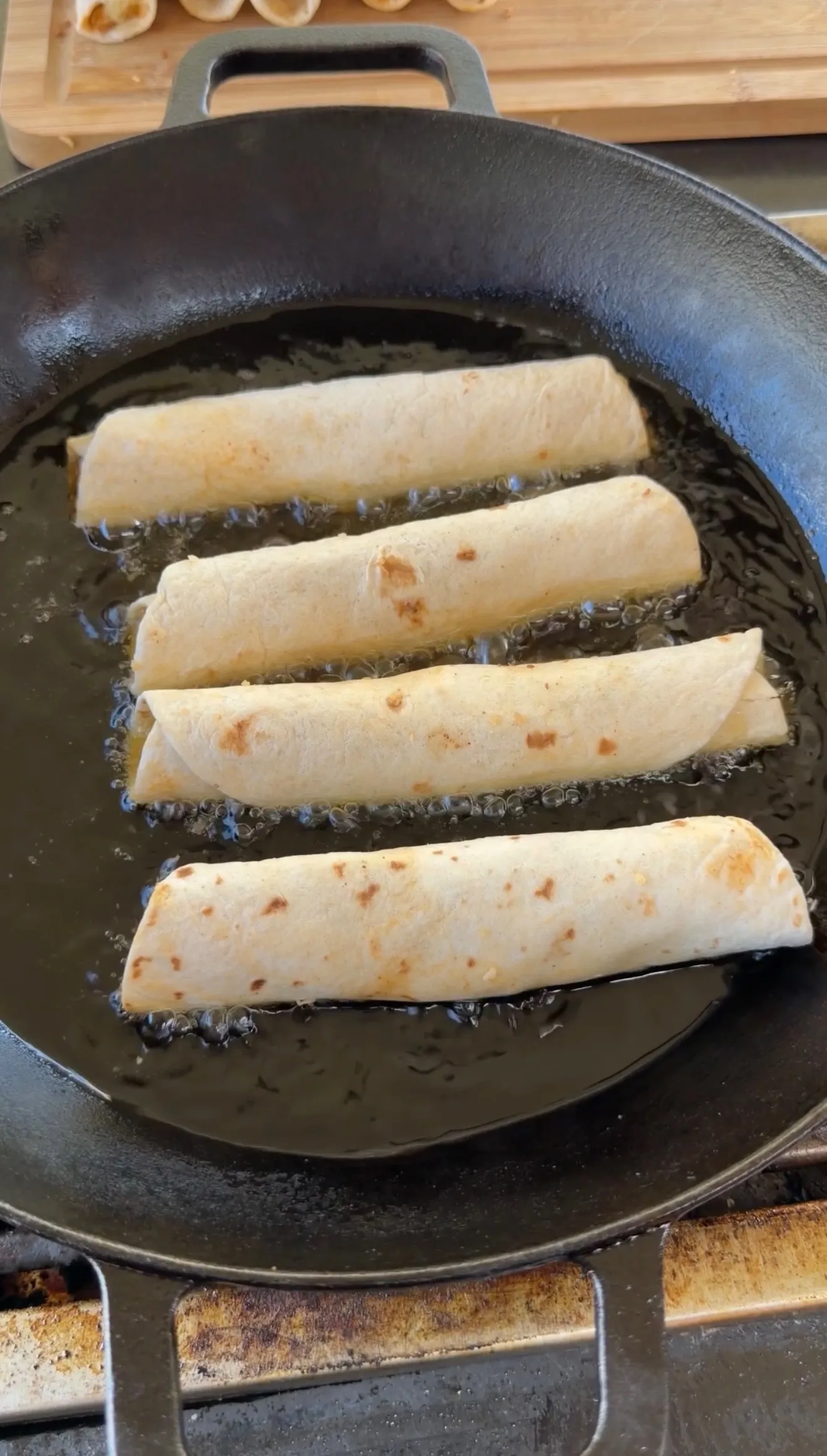 Cheesy beef taquitos frying in cast iron pan
