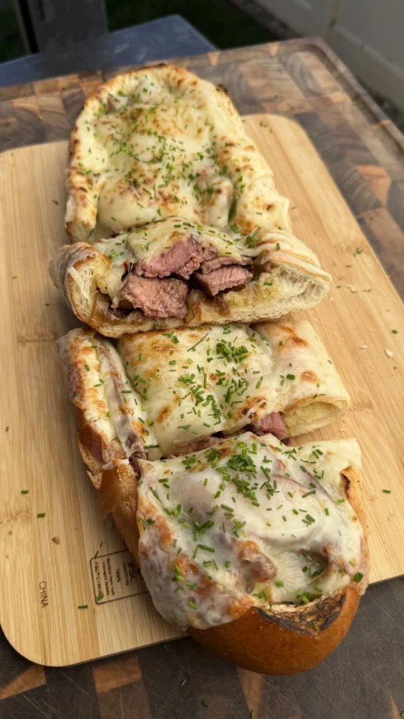 Sliced steak stuffed bread boat with melted cheese and herbs on wooden cutting board showing tender beef filling