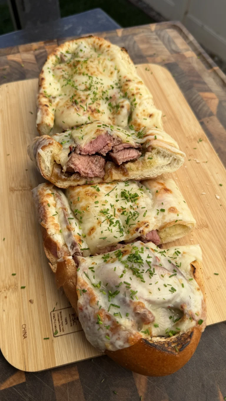 Sliced steak stuffed bread boat with melted cheese and herbs on wooden cutting board showing tender beef filling