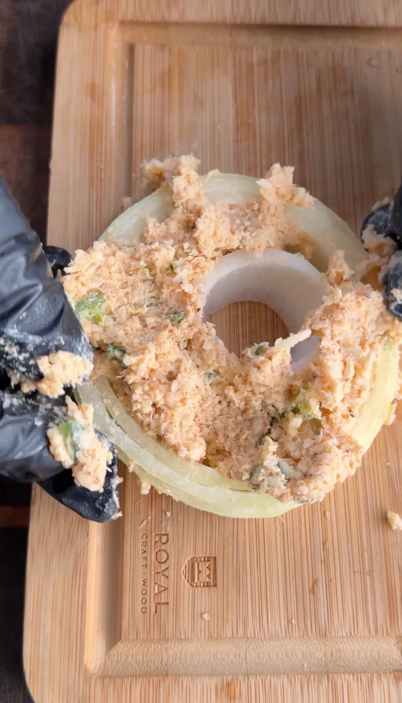 Crab stuffed onion rings being prepared on wooden cutting board with filling mixture and kitchen gloves