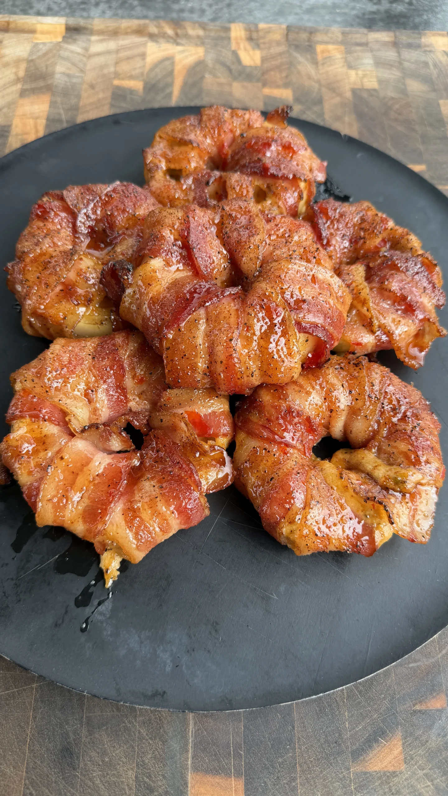 Golden brown crab stuffed bacon-wrapped onion rings arranged on a dark round plate on wooden surface