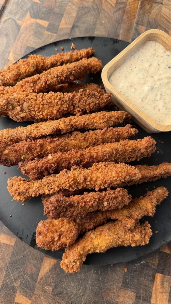 Golden crispy breaded chicken fries arranged on dark slate with creamy chipotle ranch dipping sauce