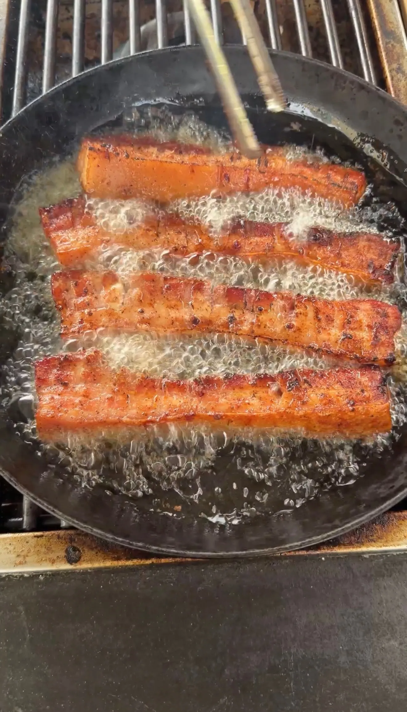 Crispy pork belly strips frying in cast iron pan