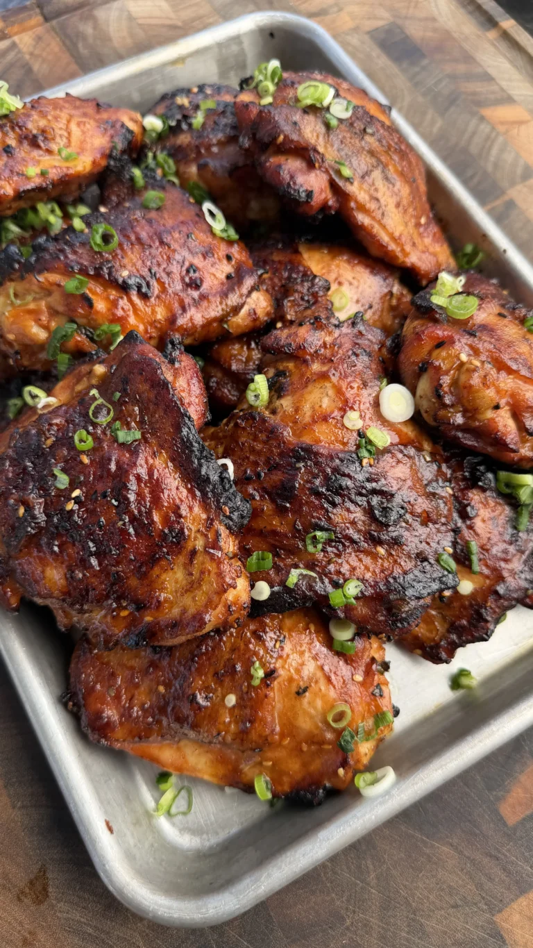 Glazed garlic chili sesame chicken thighs in white baking dish, garnished with green onions and sesame seeds