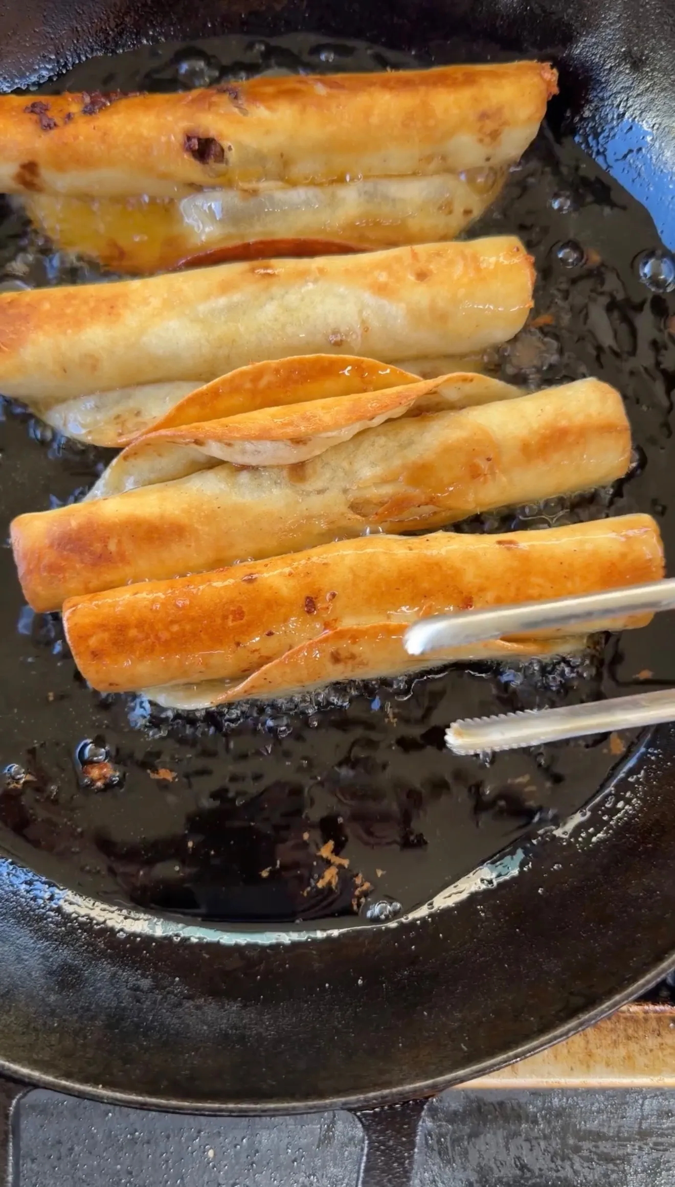 Golden beef taquitos frying in cast iron pan