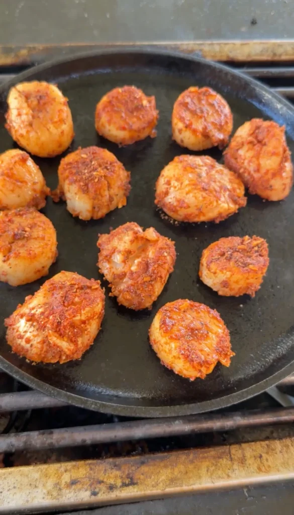 Golden brown seared scallops cooking in a black cast iron skillet on stovetop