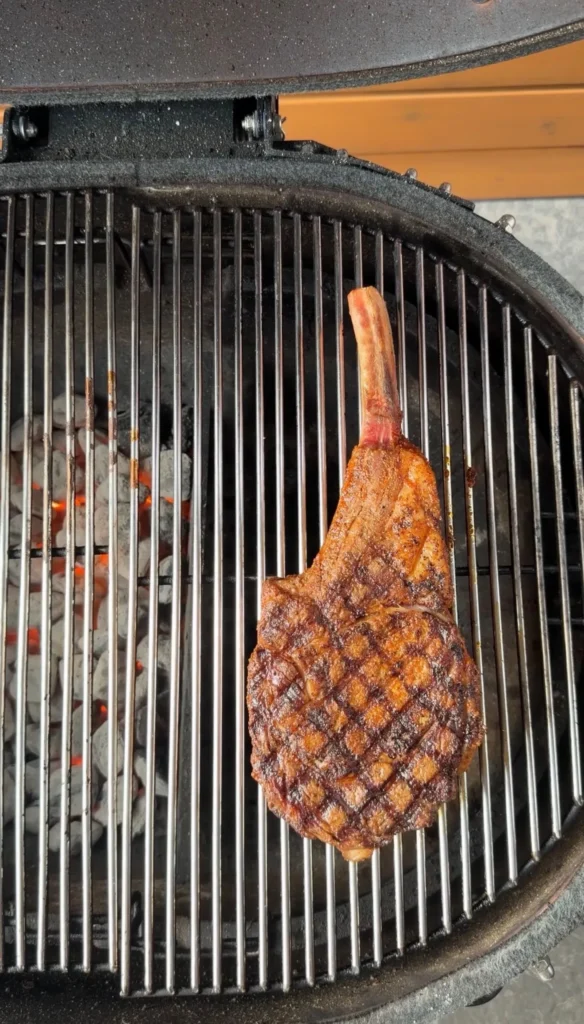 Grilled cowboy ribeye steak with crosshatch grill marks cooking on round barbecue grill grates