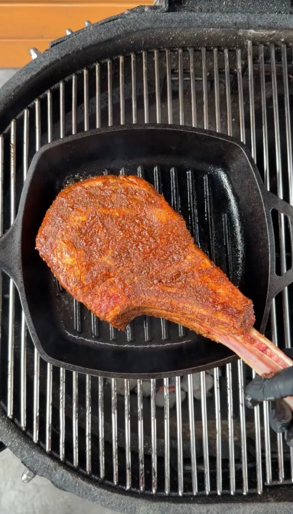 Grilled cowboy ribeye steak with glossy worcestershire glaze cooking in cast iron pan on outdoor grill grates