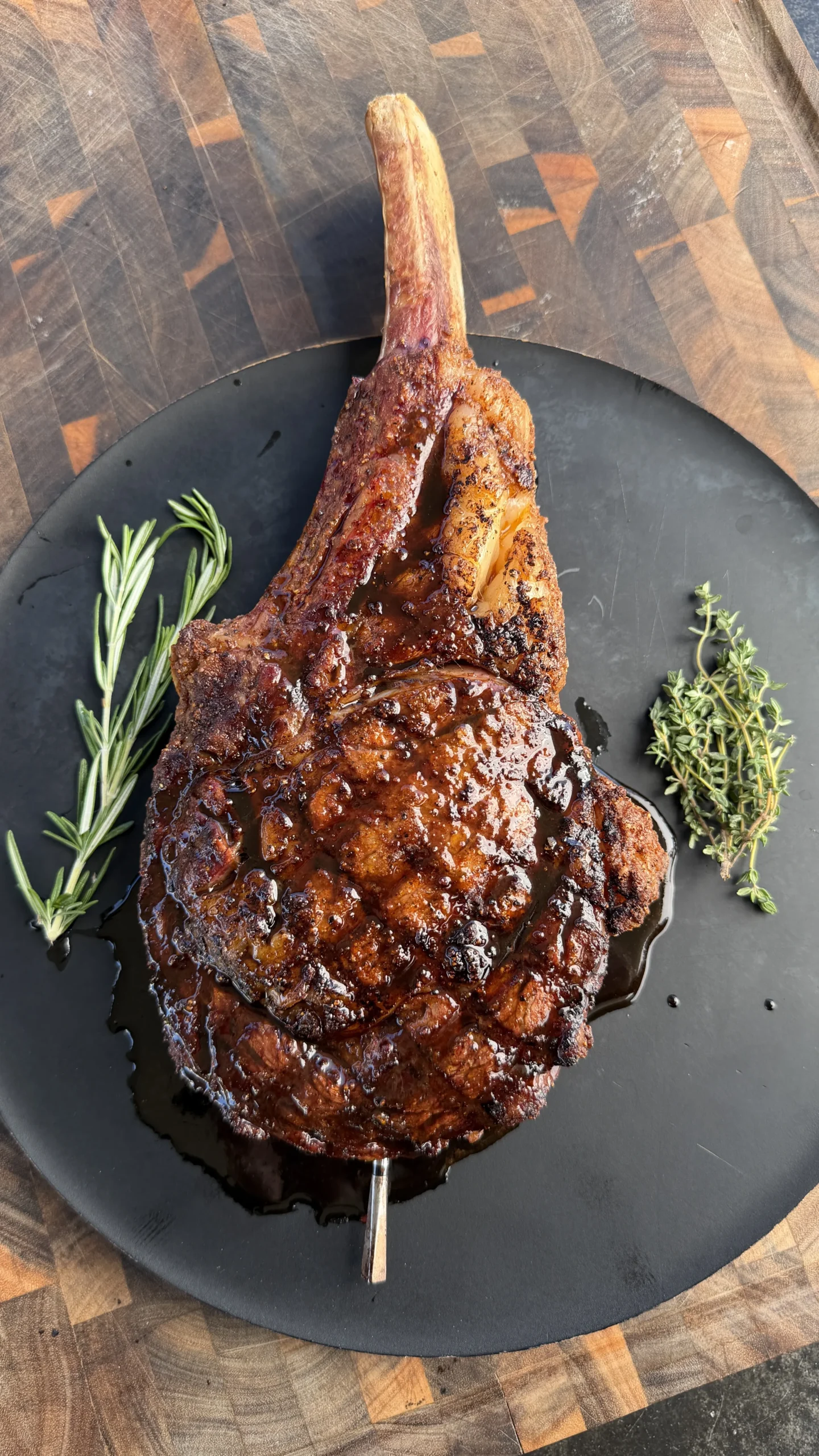 Grilled cowboy ribeye steak with glossy Worcestershire glaze on black cast iron plate with fresh herbs