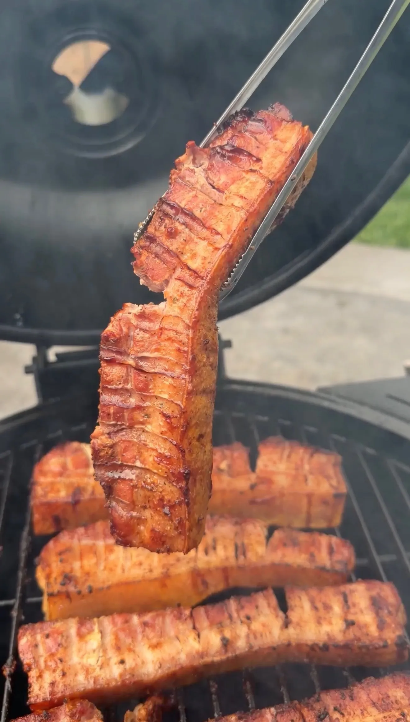 Grilled pork belly strips with tongs on barbecue