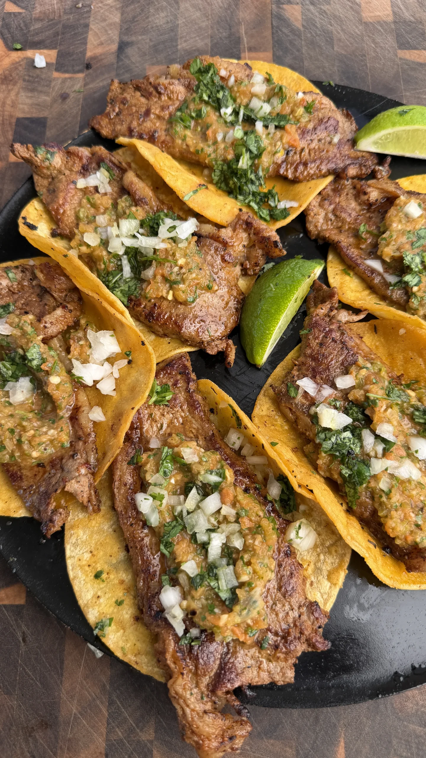 Grilled steak tacos with charred salsa, diced onions, and cilantro on corn tortillas served on a black slate plate