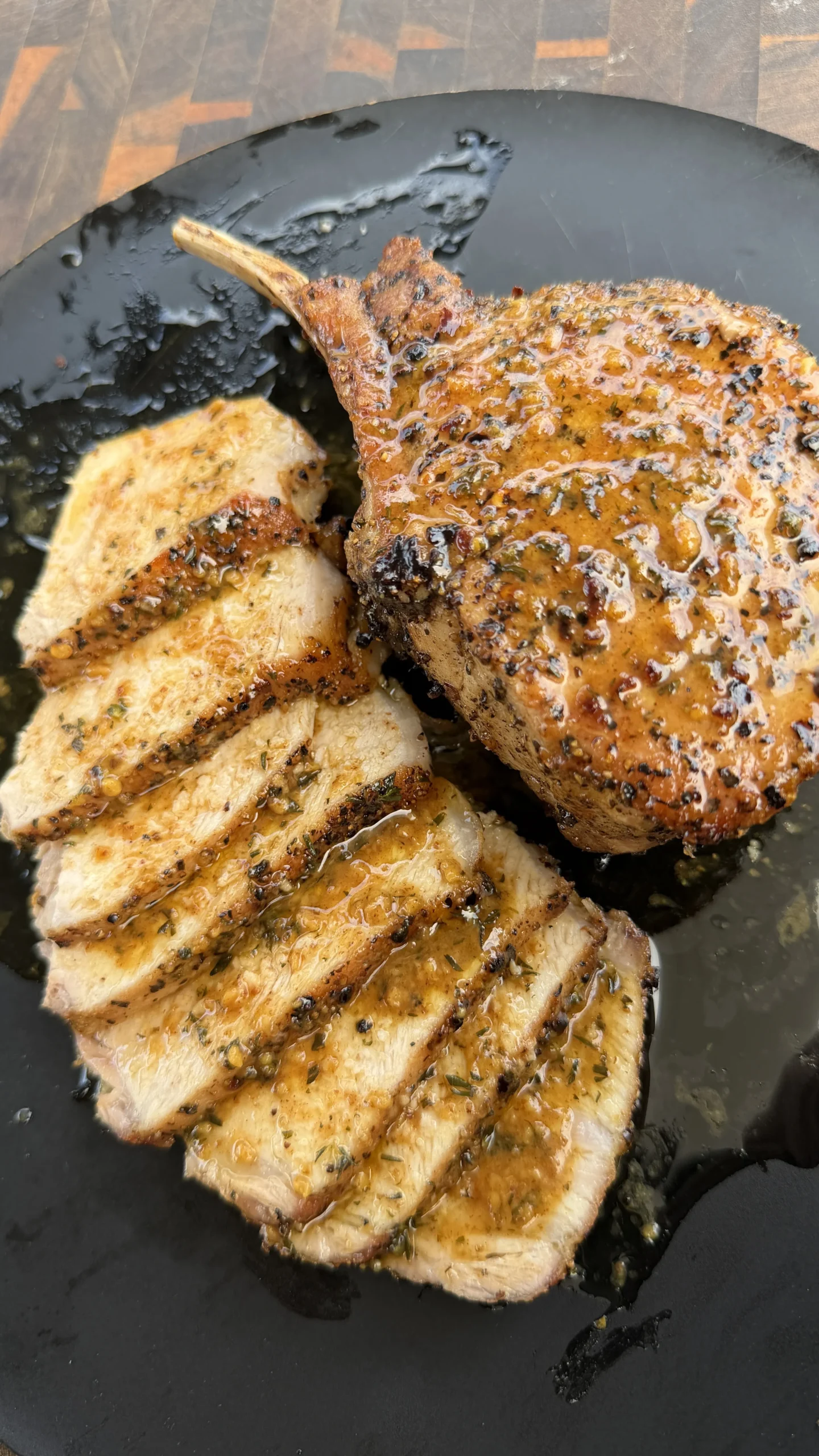 Pan-seared double bone pork chops with golden crust, one sliced showing juicy interior, in dark cast iron pan