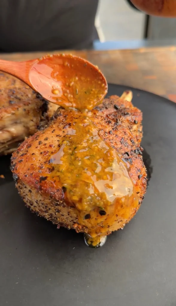 Golden-brown seared double bone pork chops being basted with garlic herb butter sauce from a wooden spoon