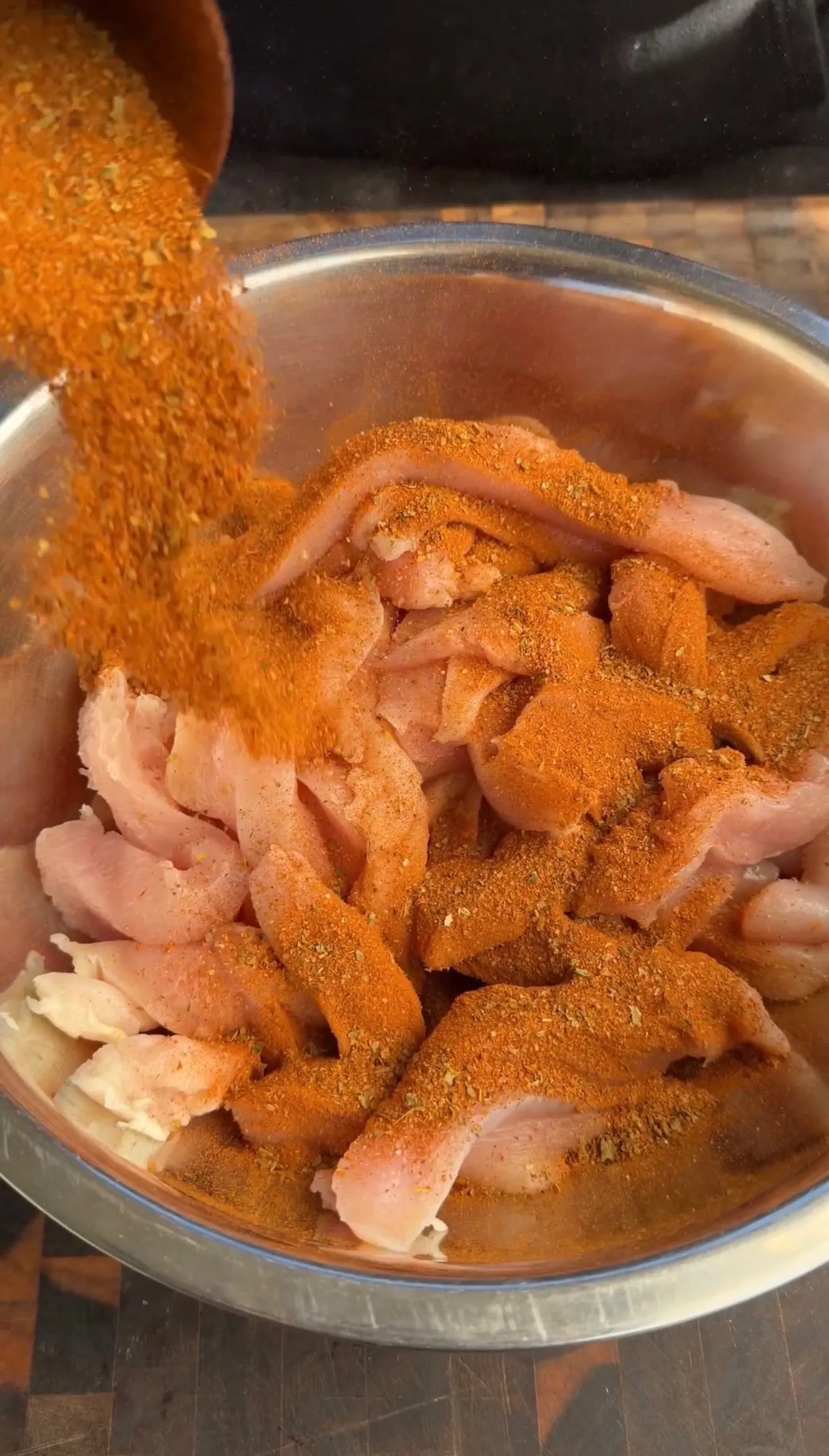 Raw chicken strips seasoned with spices in bowl