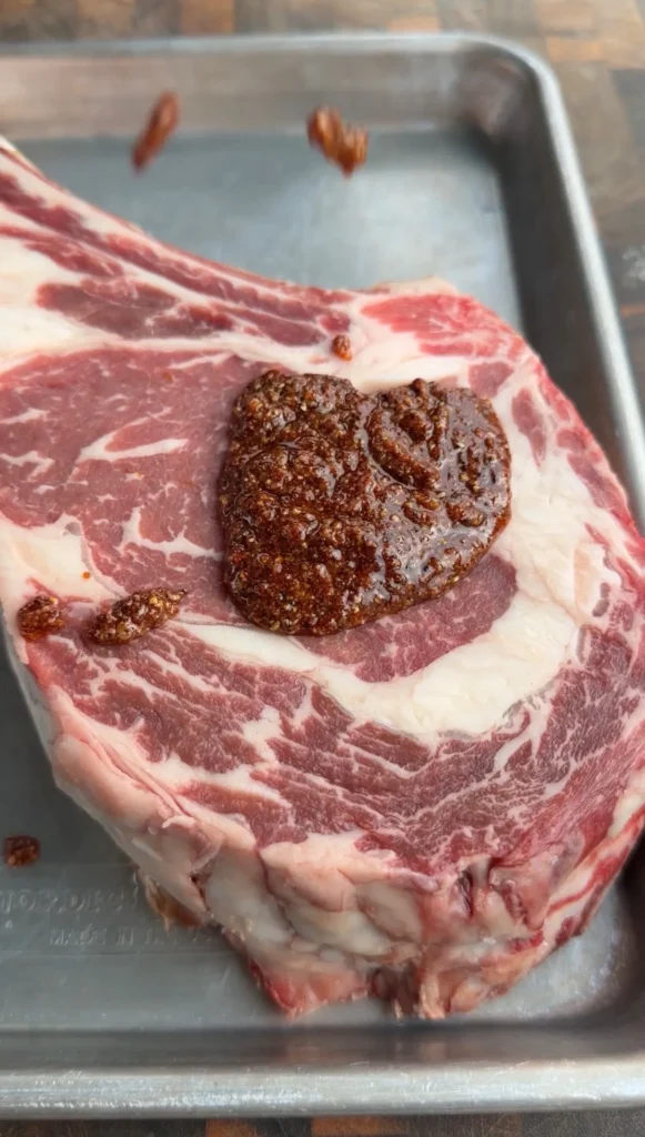 Raw cowboy ribeye steak with dark worcestershire glaze on metal baking sheet ready for cooking