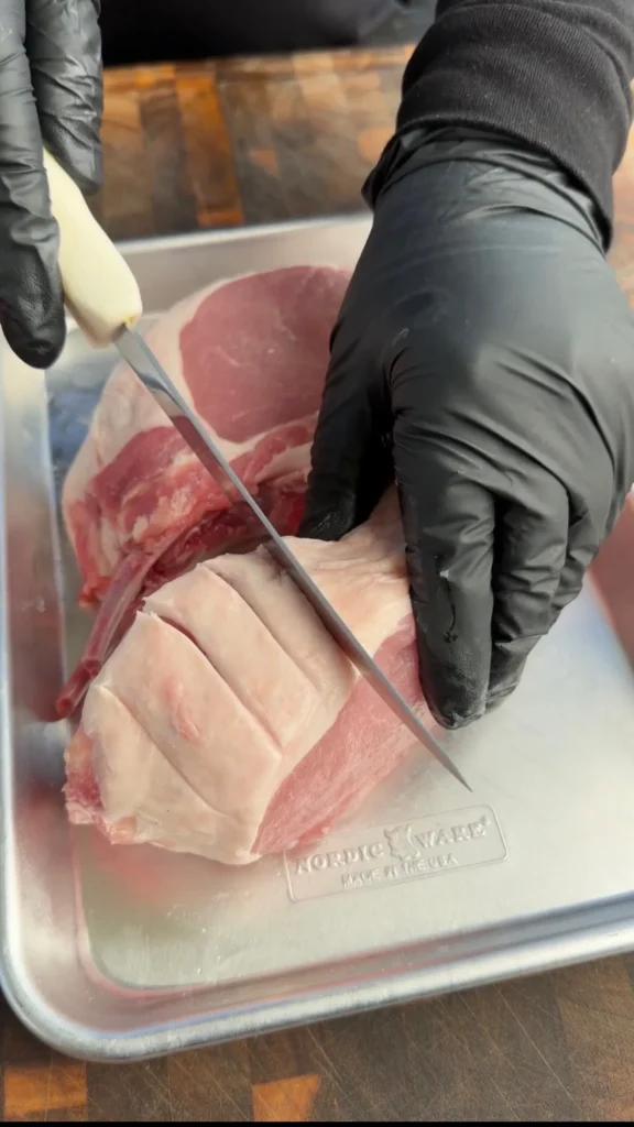 Hands in black gloves scoring raw double bone pork chops with a knife on a cutting board