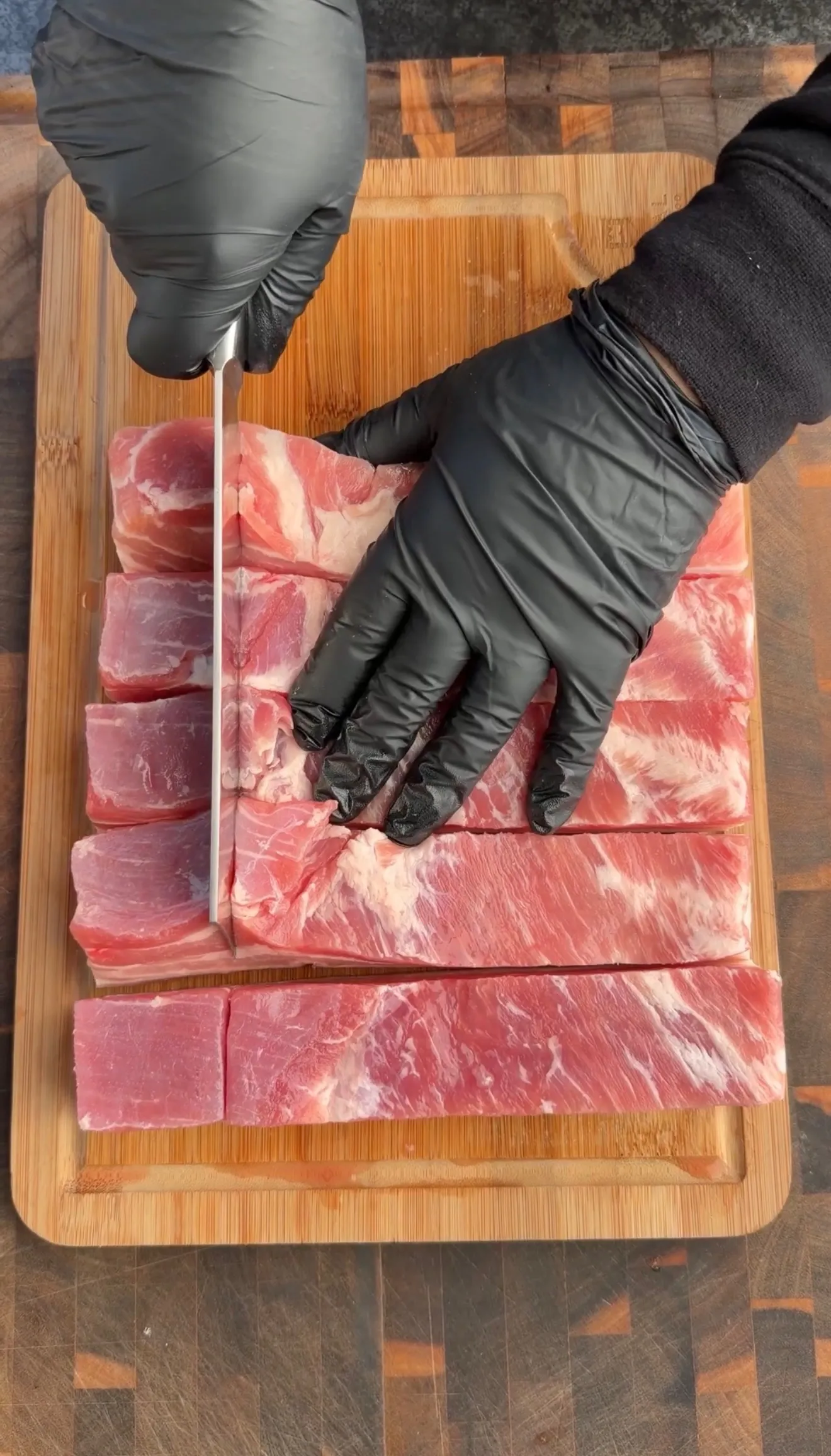 Raw pork belly being cut on cutting board