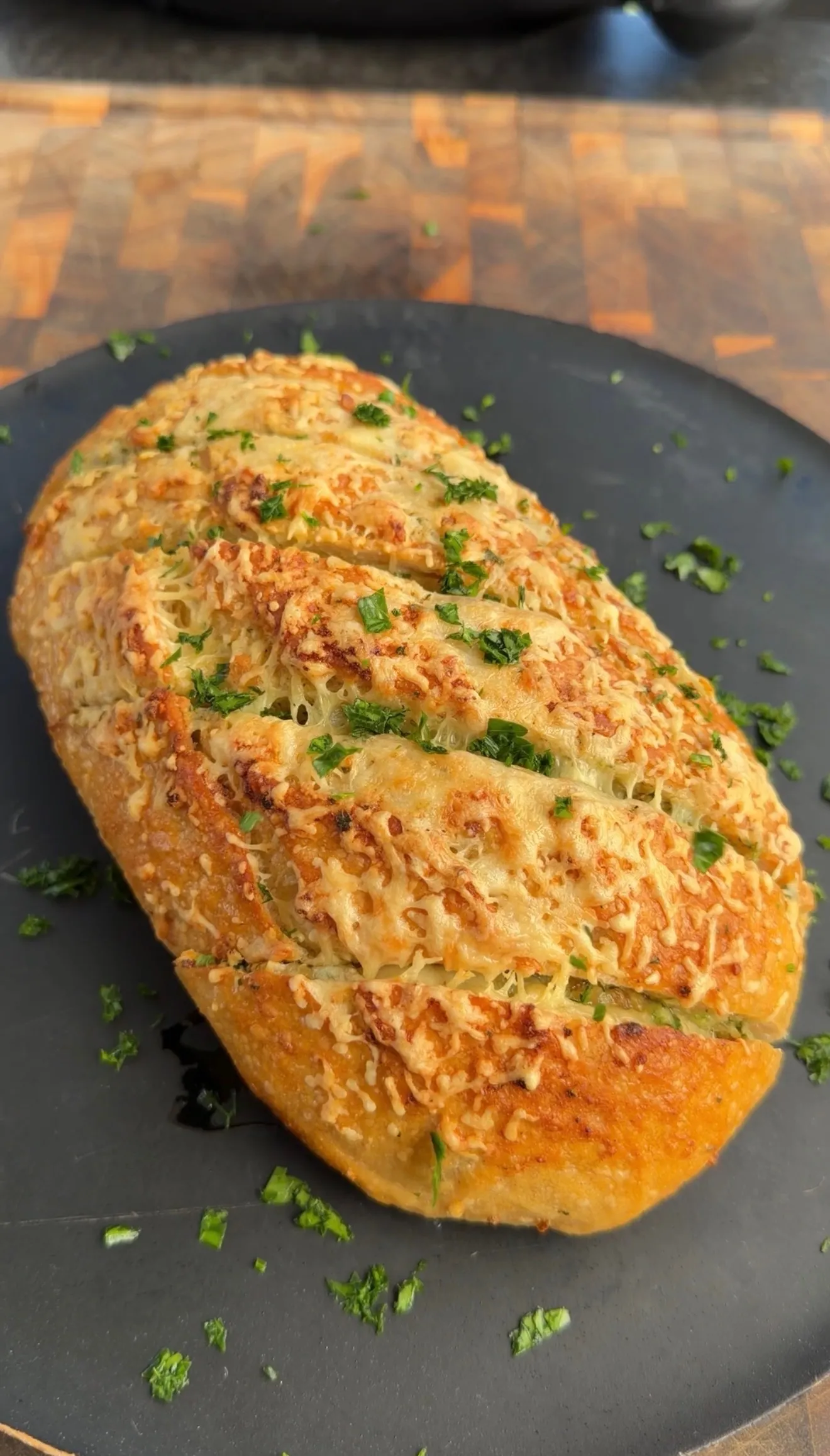 Sliced roasted garlic parmesan pull-apart sourdough bread with melted cheese and fresh herbs on dark plate