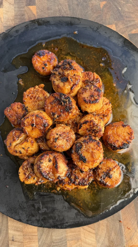 Golden brown seared scallops with caramelized crust in a dark cast iron skillet with cooking juices