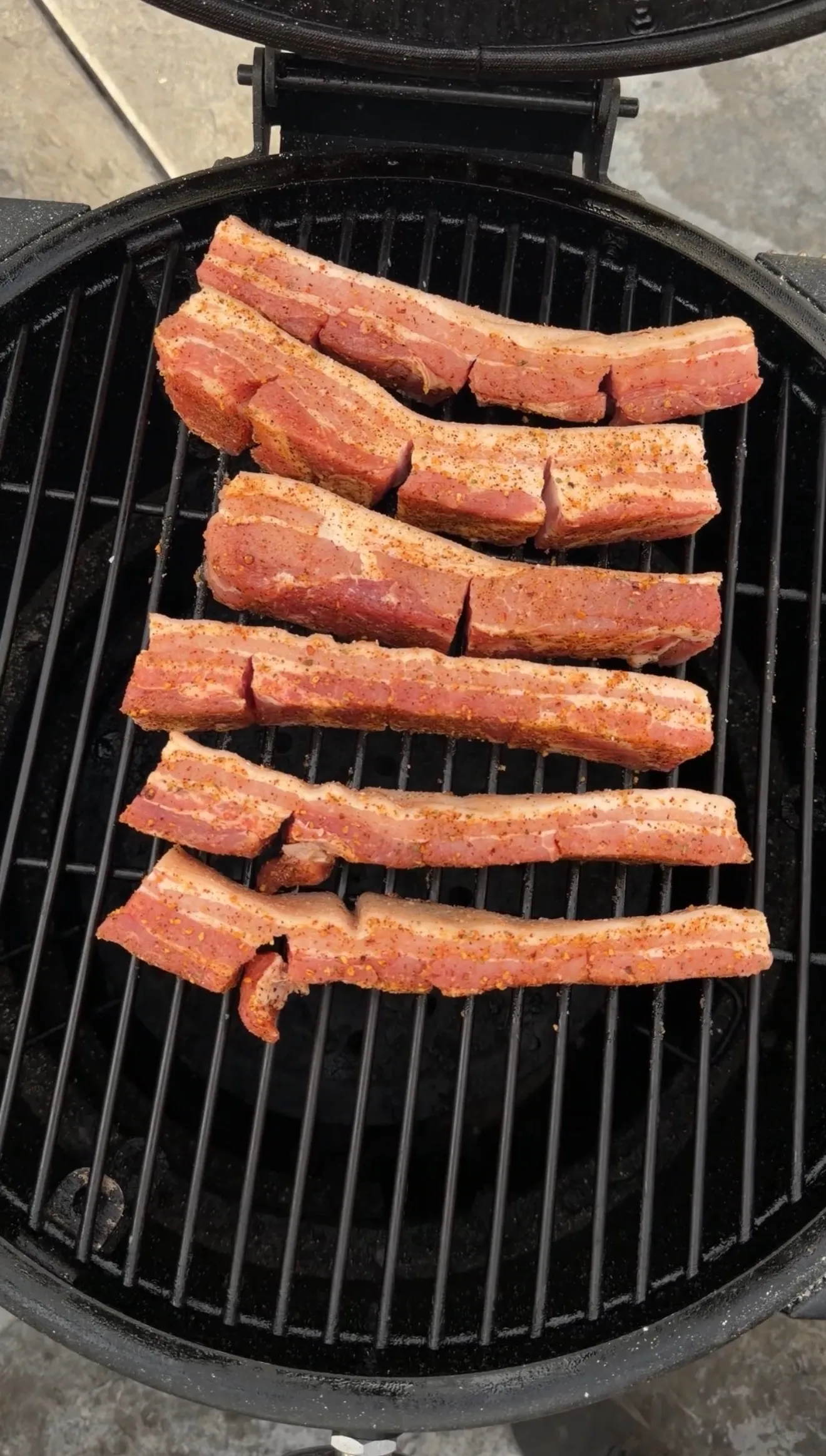 Seasoned pork belly strips smoking on grill
