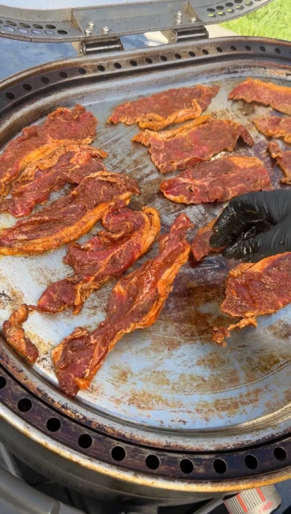 Seasoned steak pieces with red marinade cooking on a round outdoor grill for steak tacos