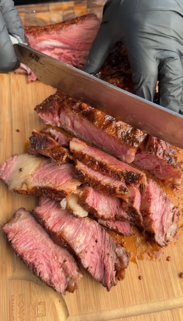 Sliced cowboy ribeye steak with dark worcestershire glaze on wooden cutting board, showing medium-rare interior