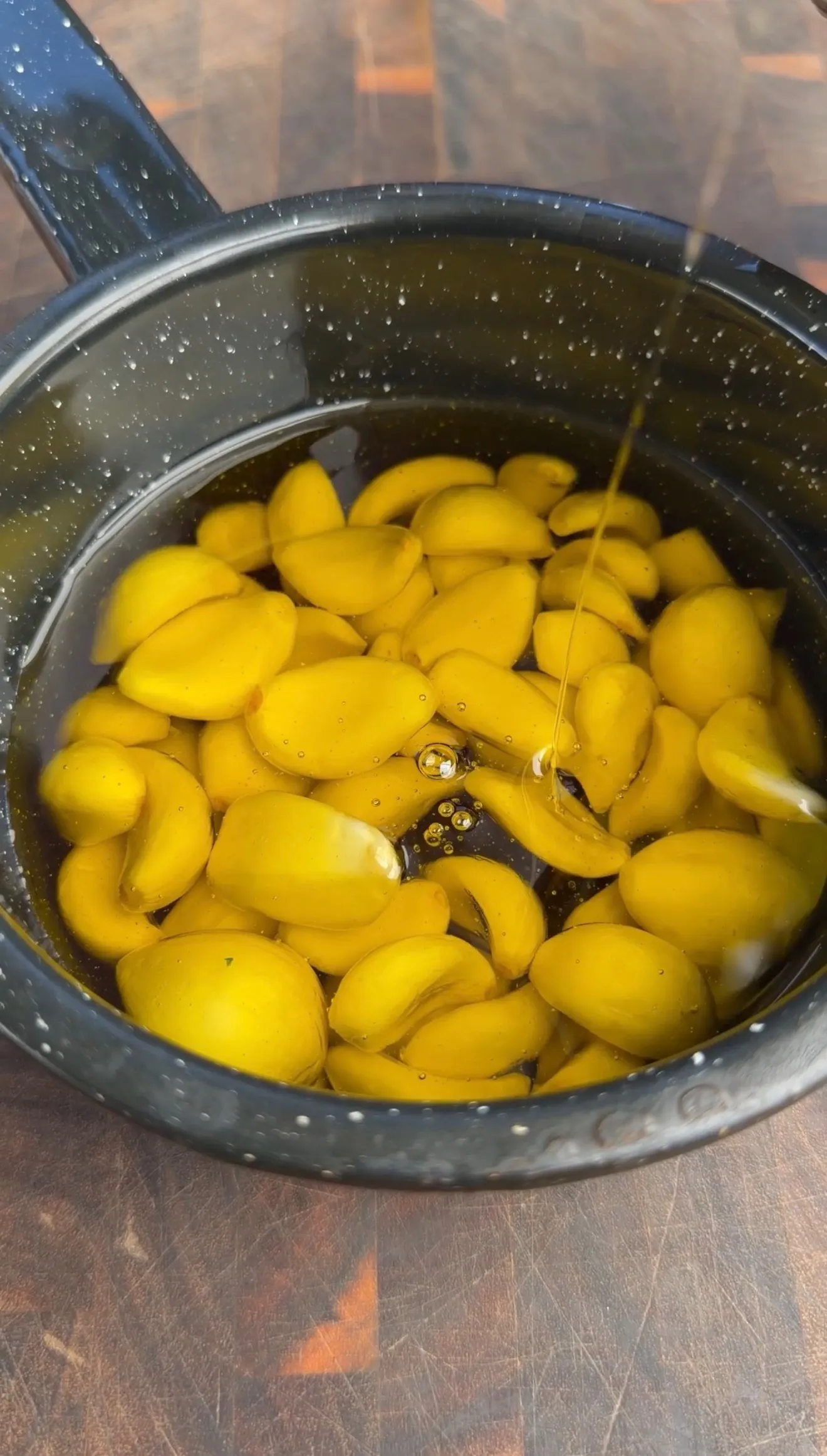 Garlic cloves cooking slowly in oil in speckled pan