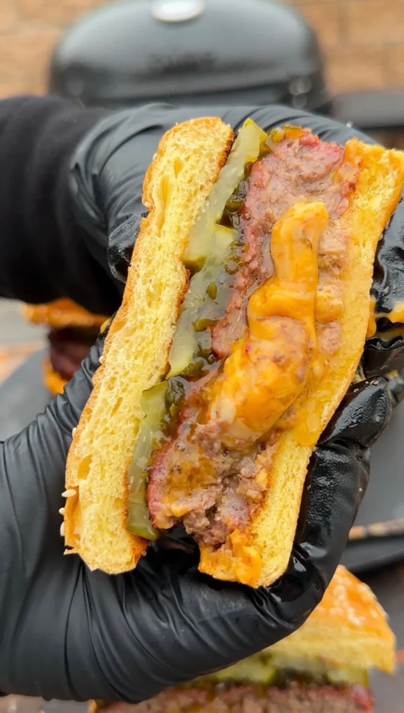 Cross-section of Spicy Juicy Lucy burger held in gloved hands showing melted cheese, bacon, and jalapeños