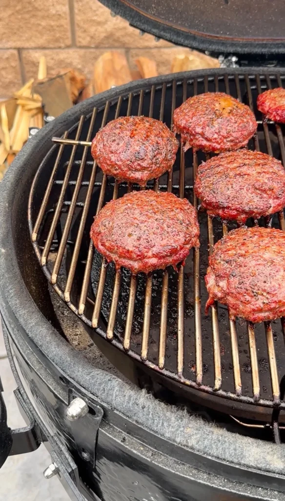 Spicy Juicy Lucy burger patties with melted cheese centers cooking on a kamado grill grates