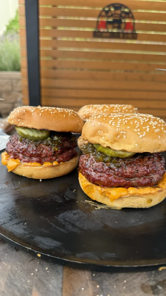 Spicy Juicy Lucy burgers with melted cheese, pickles, and sesame seed buns on a dark slate serving board
