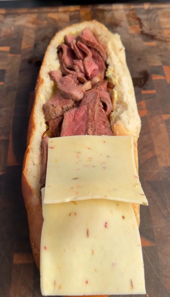 Steak stuffed bread boat filled with tender beef and topped with sliced cheese on wooden cutting board