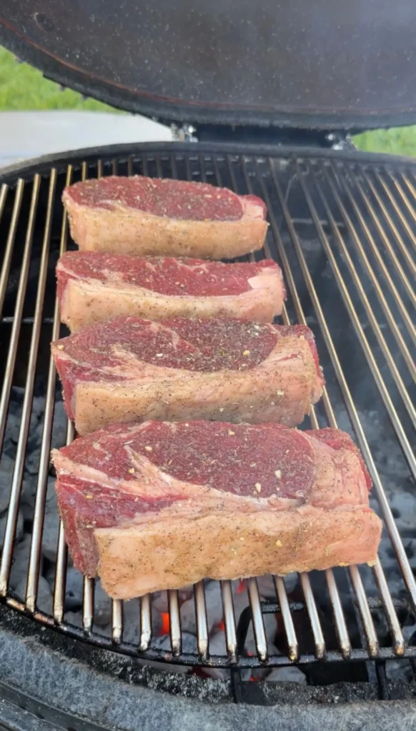 Four steak stuffed bread boats seasoned with herbs grilling on outdoor barbecue grates with visible flames