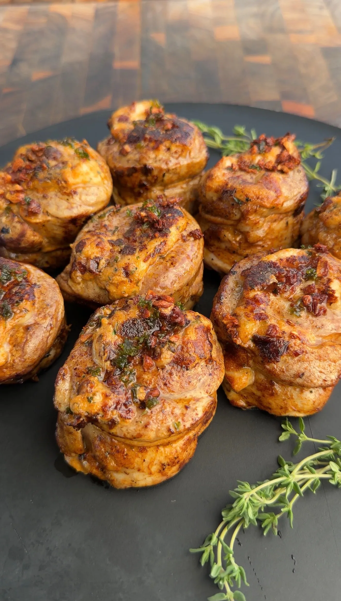 Golden-brown stuffed pork tenderloin pinwheels arranged on dark plate, garnished with fresh thyme
