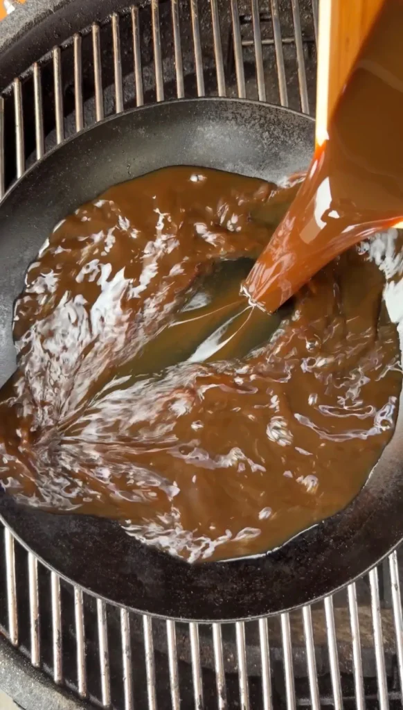 Rich brown Worcestershire glaze bubbling and simmering in a black cast iron skillet with wooden spoon