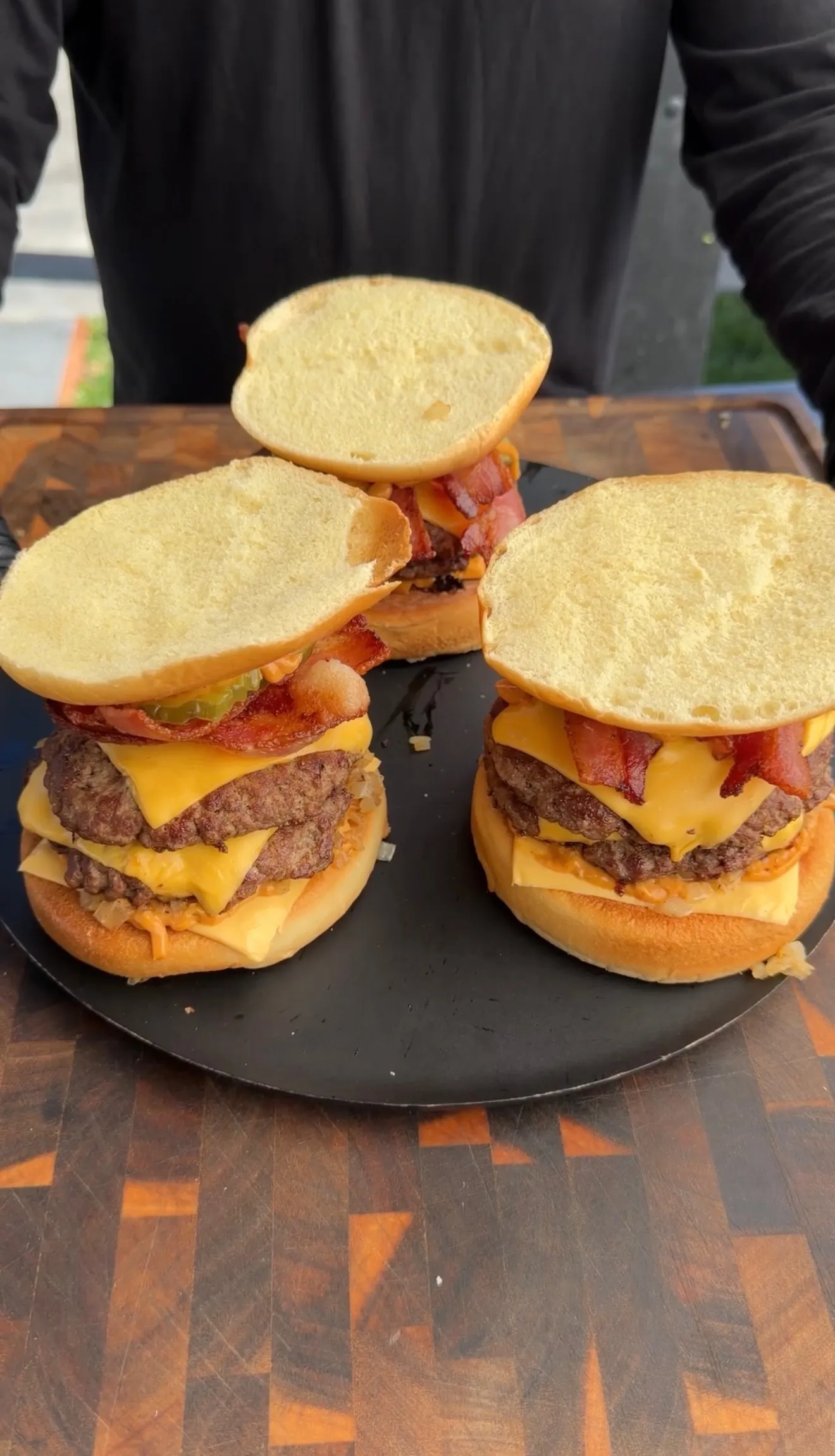 Two bacon cheeseburger patty melts cut in half on a dark plate, showing layers of beef, cheese, and bacon