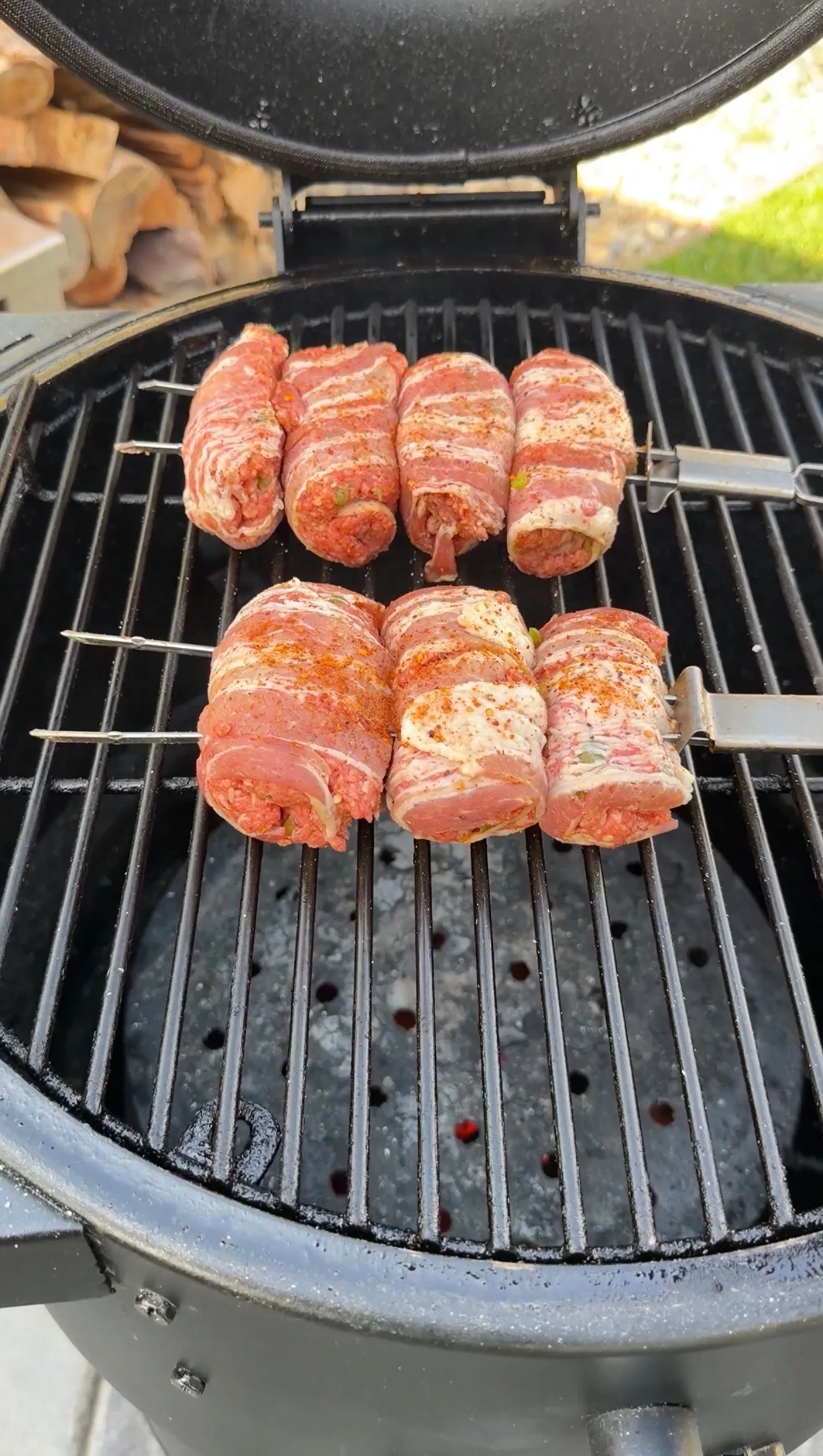 Bacon-wrapped jalapeño beef skewers cooking on a kamado grill with charcoal grates