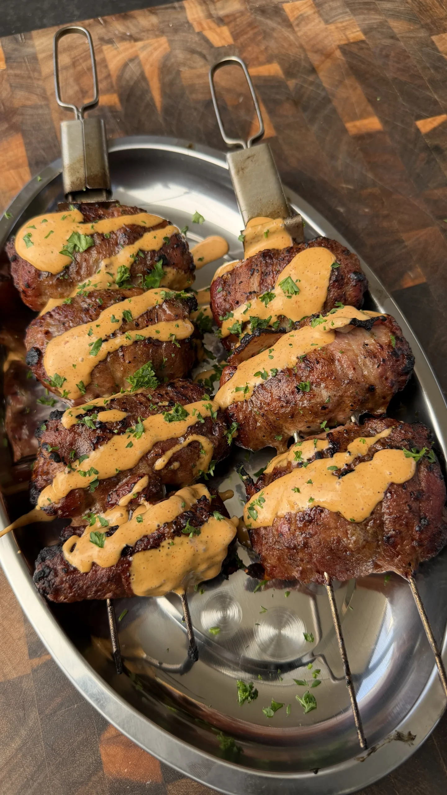 Bacon-wrapped jalapeño beef skewers on metal platter drizzled with orange sauce and fresh herbs