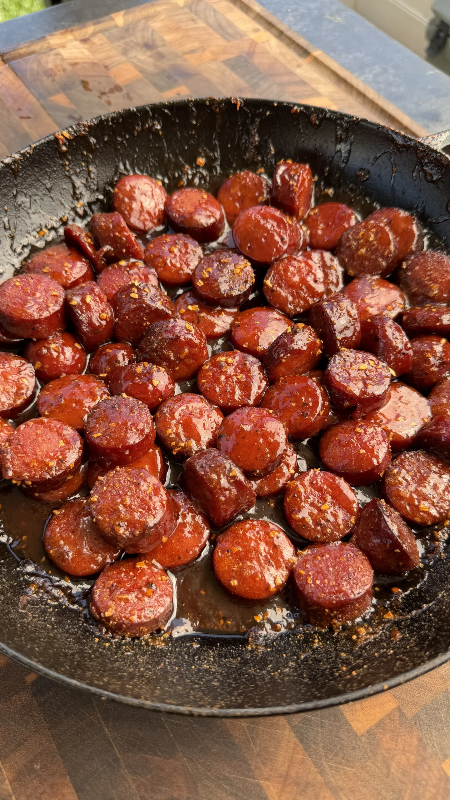 BBQ smoked sausage burnt ends with caramelized glaze cooking in a seasoned cast iron skillet