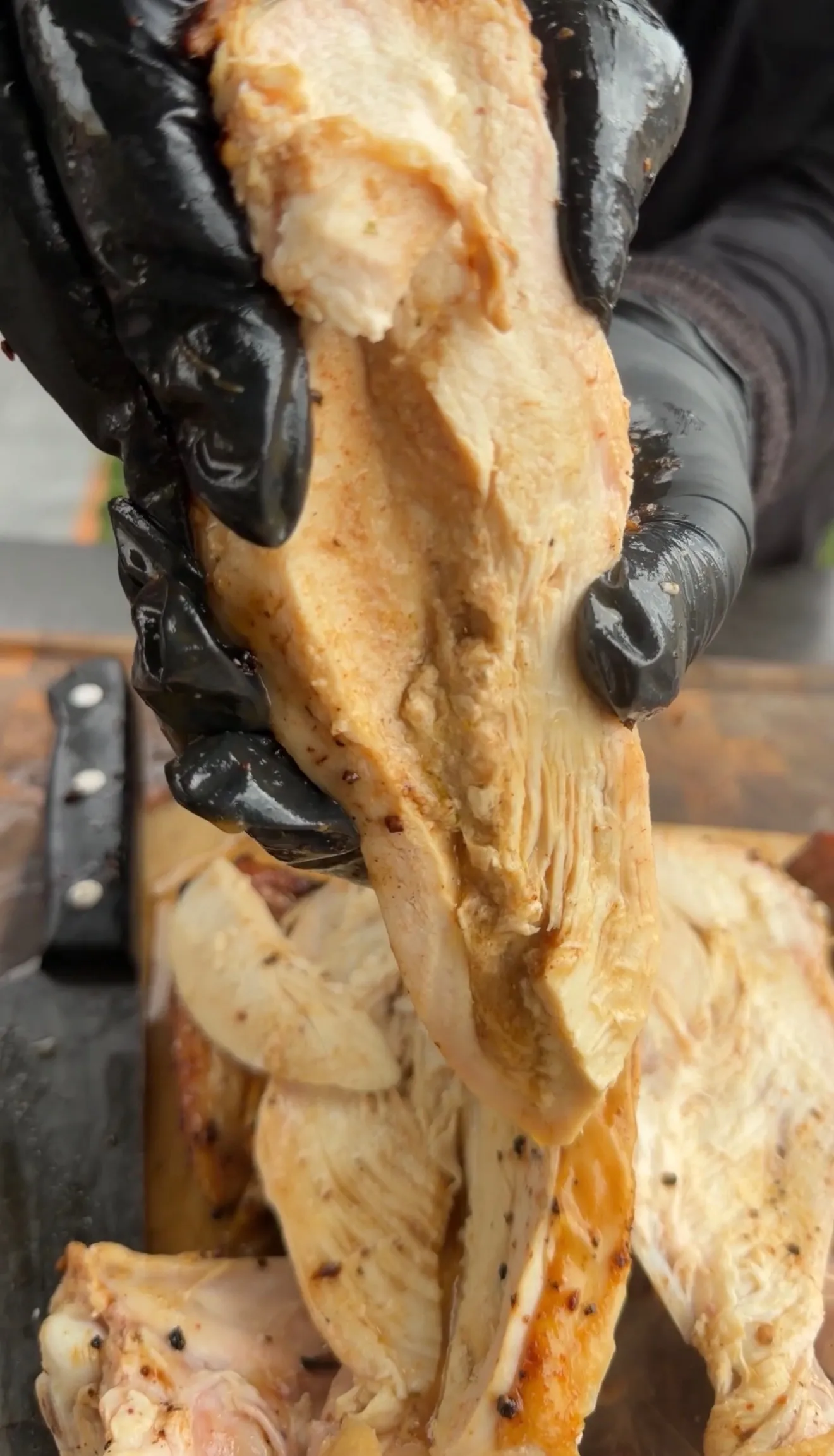 Hands in black gloves using tongs to carve golden-brown beer can chicken, showing tender juicy meat