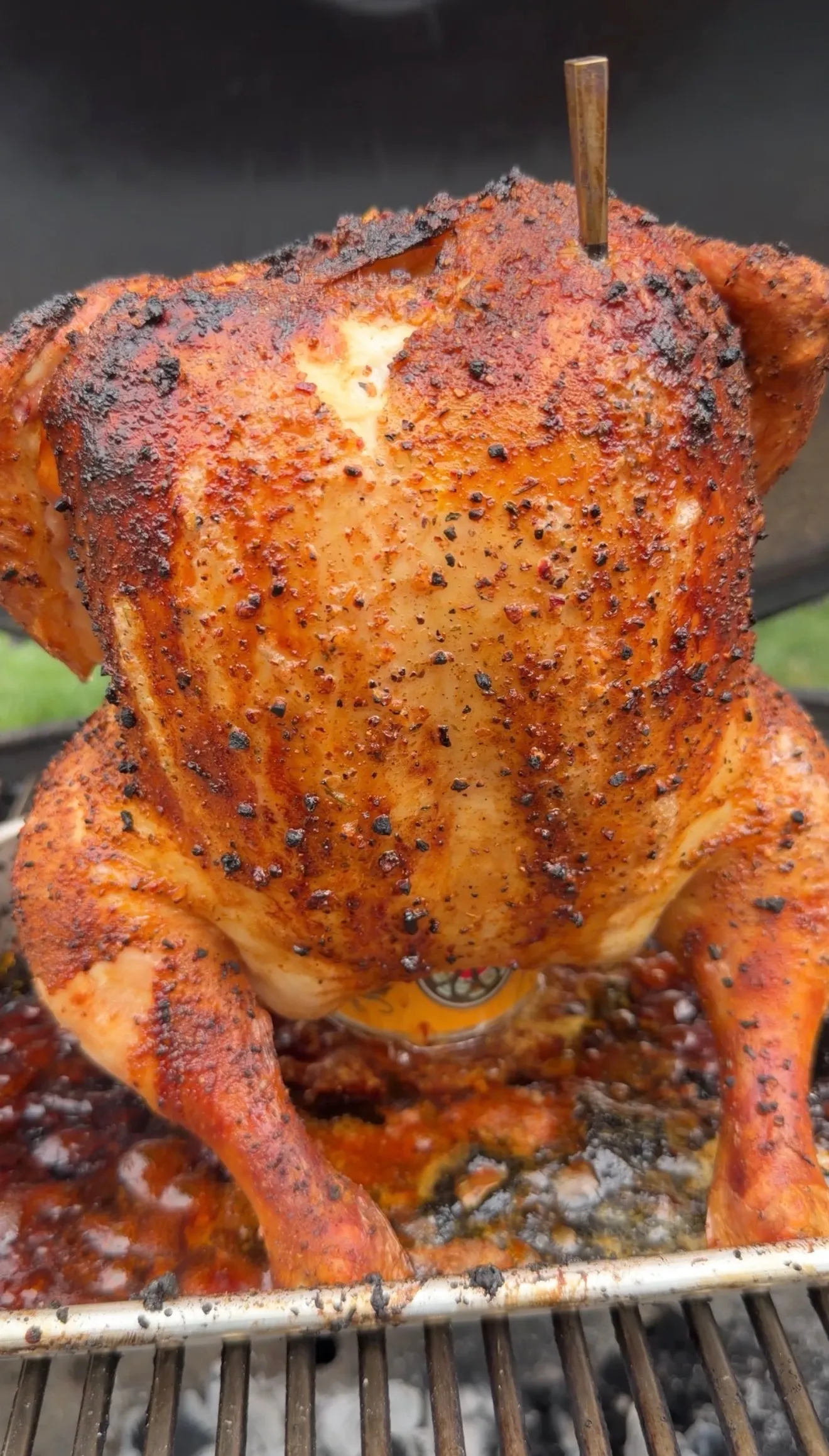 Seasoned beer can chicken cooking upright on a barbecue grill with golden crispy skin and black pepper rub