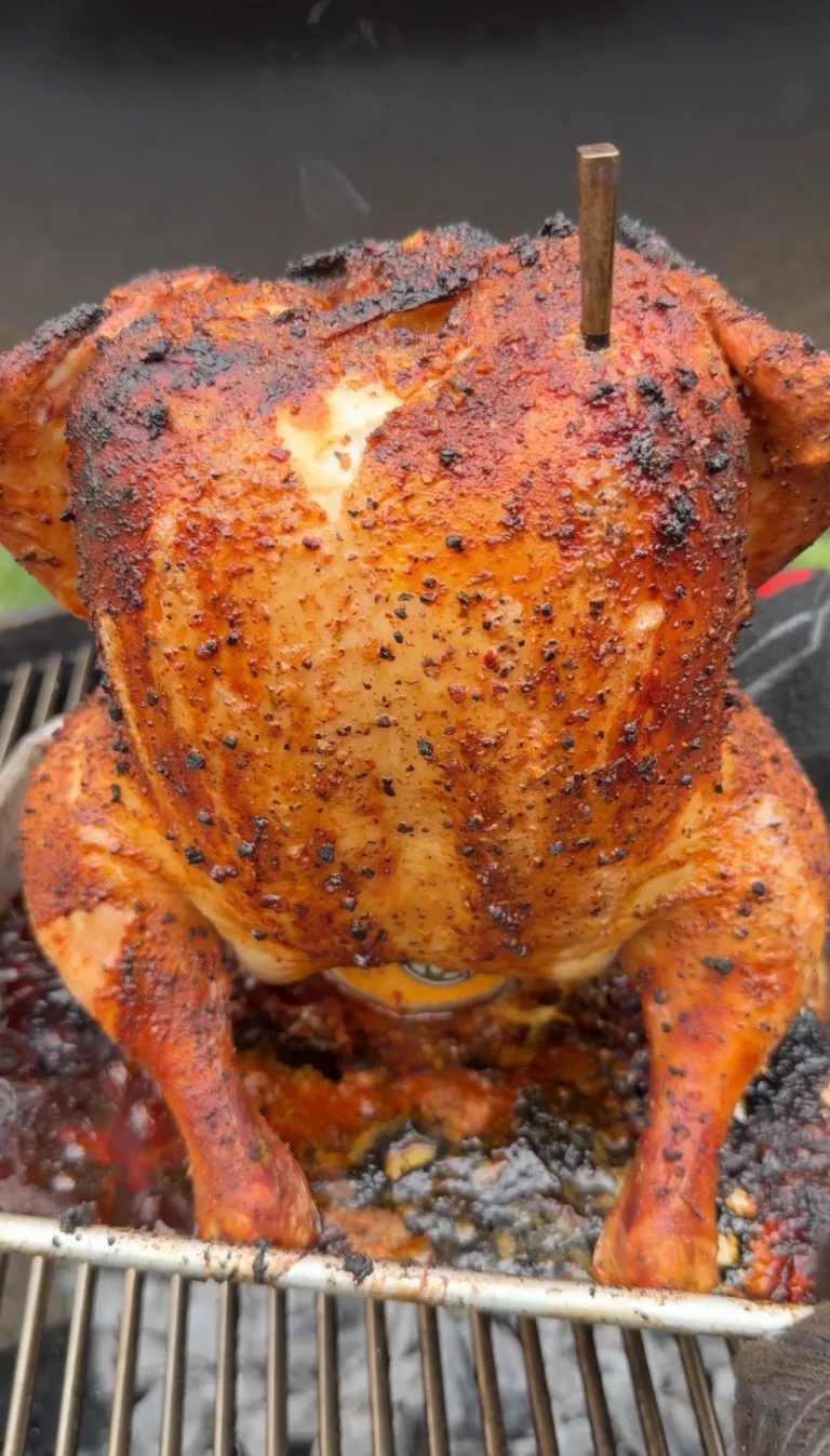 Beer can chicken with golden crispy skin and seasoning cooking upright on a barbecue grill grate