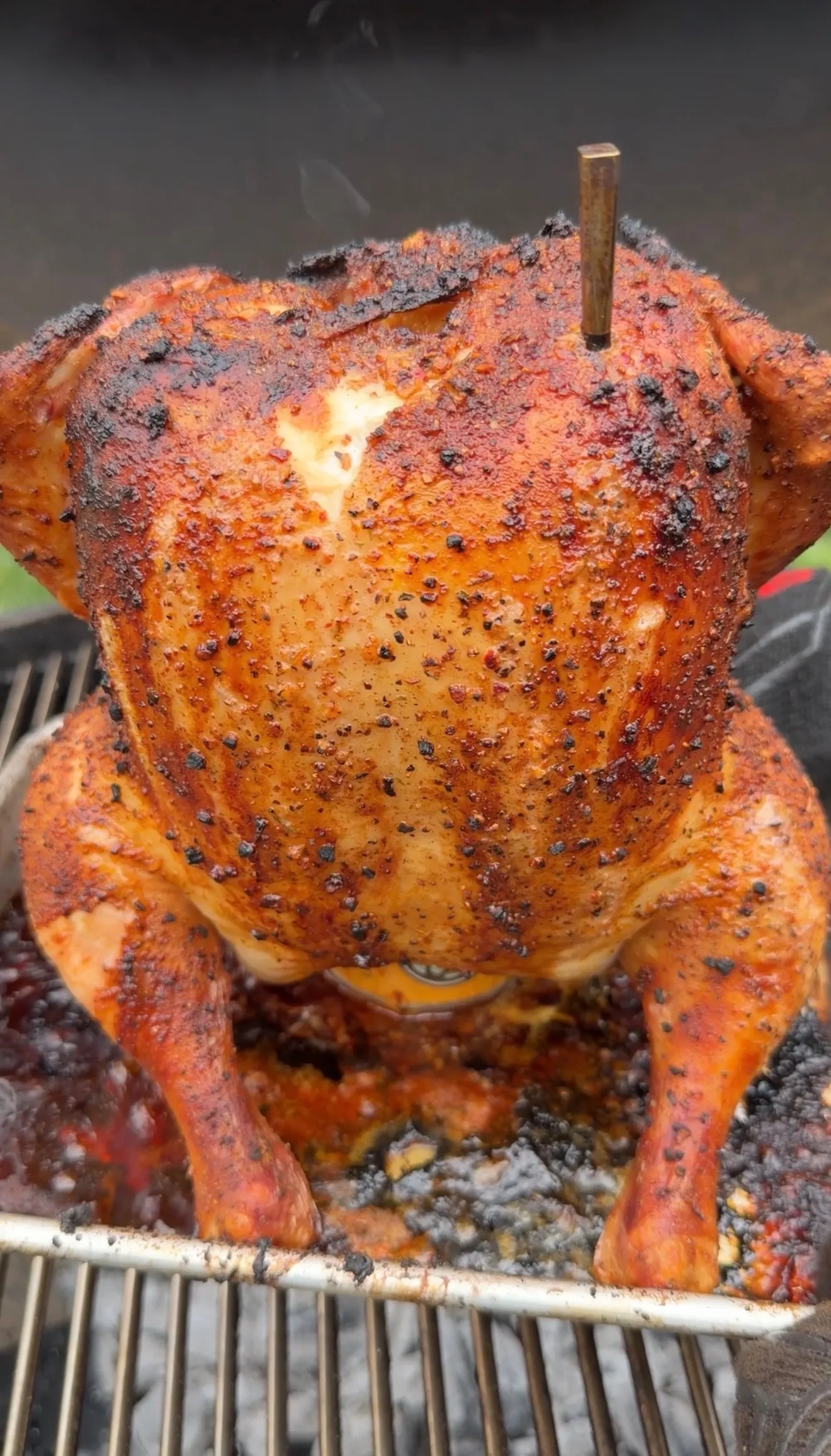 Beer can chicken with golden crispy skin and seasoning cooking upright on a barbecue grill grate