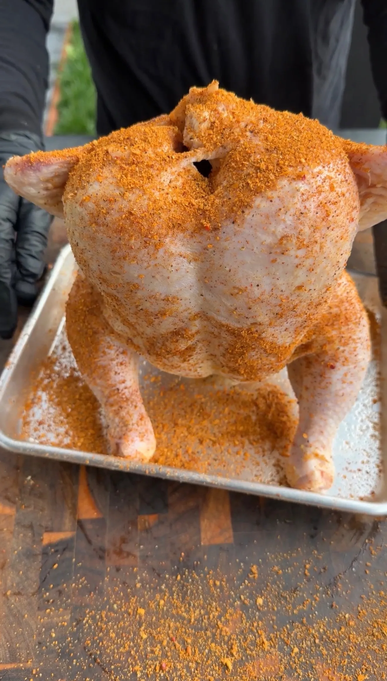 Raw whole chicken heavily coated in orange paprika spice rub positioned over beer can on metal tray
