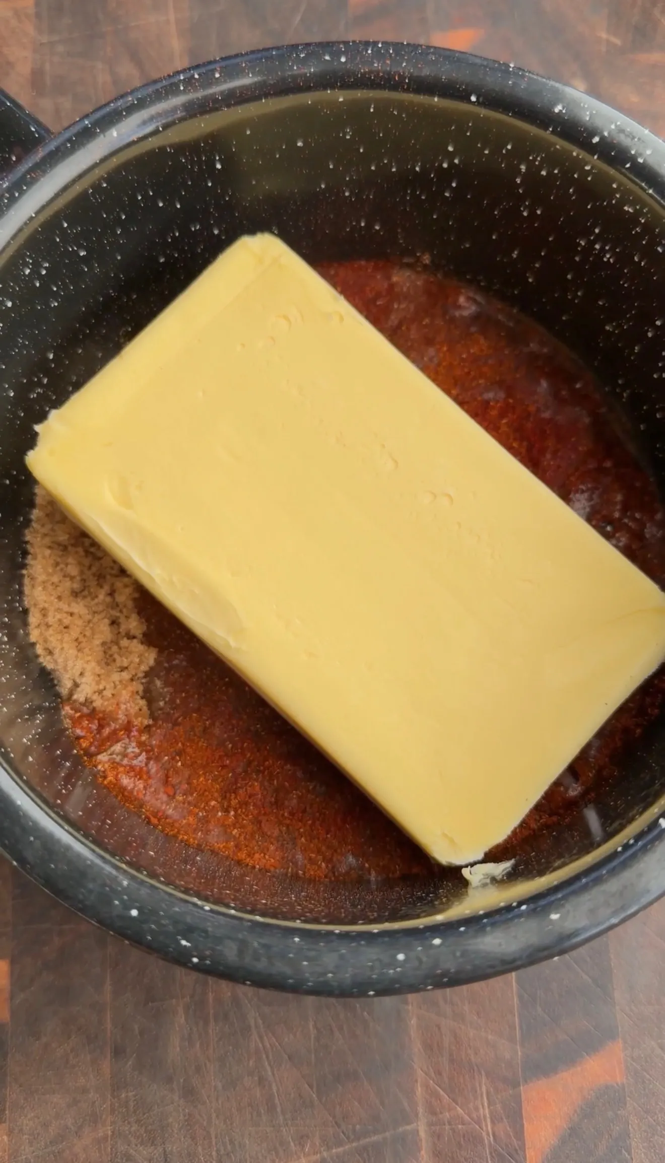 Stick of butter melting in a black speckled pan with brown seasonings for Nashville hot pickle brined wings