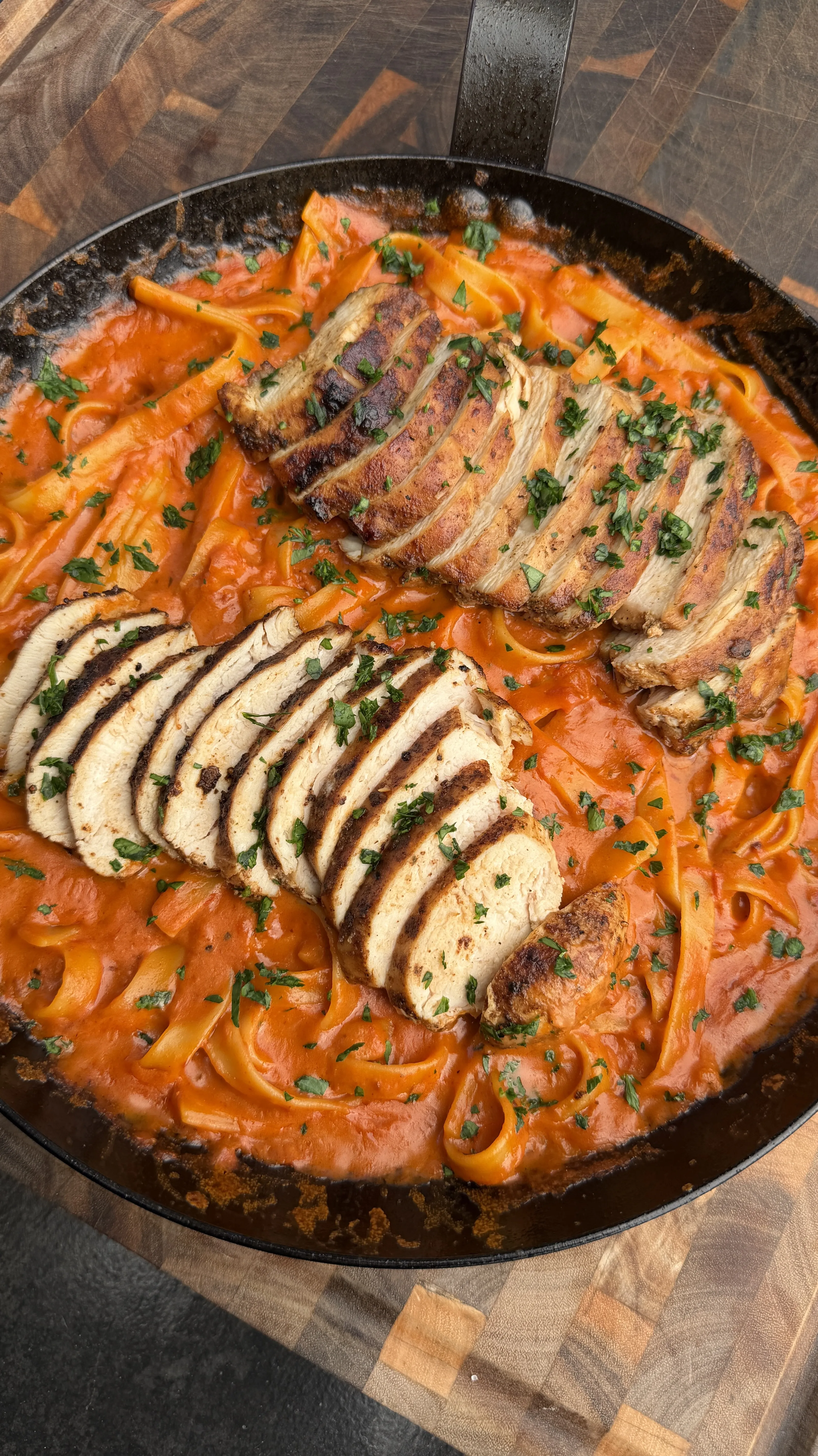 Sliced Cajun chicken fettuccine with red pepper sauce in a black cast iron skillet garnished with fresh herbs
