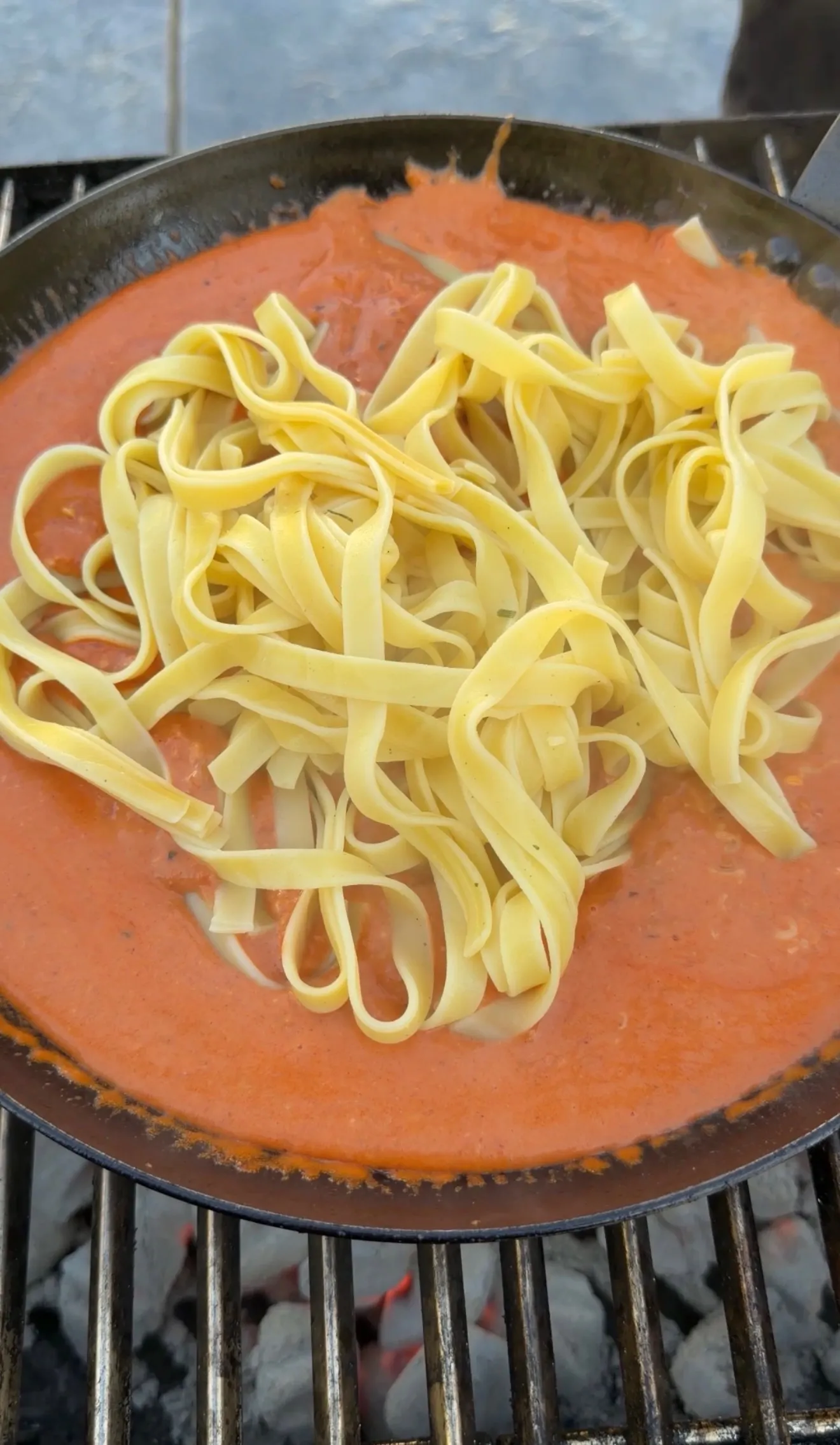 Fettuccine pasta being tossed in creamy tomato sauce in a black skillet pan during cooking